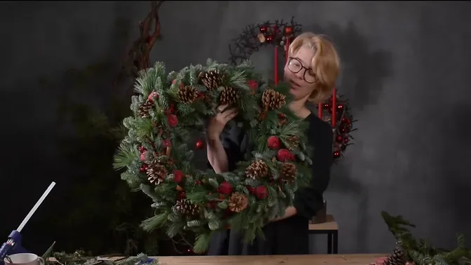 Separate evergreen wreath with red decorative apples, pinecones and cinnamon held upright
