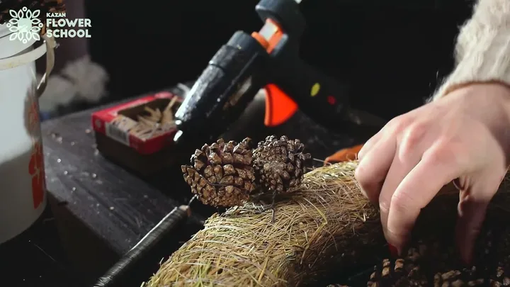A pinecone sits on the hay ring with wire around its lower scales.