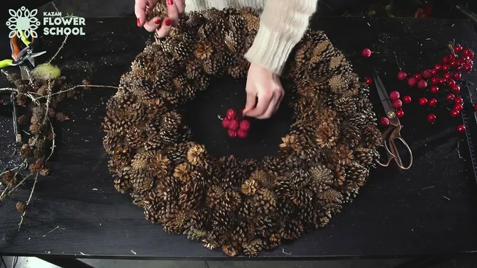 A red berry cluster being positioned above the pinecone wreath