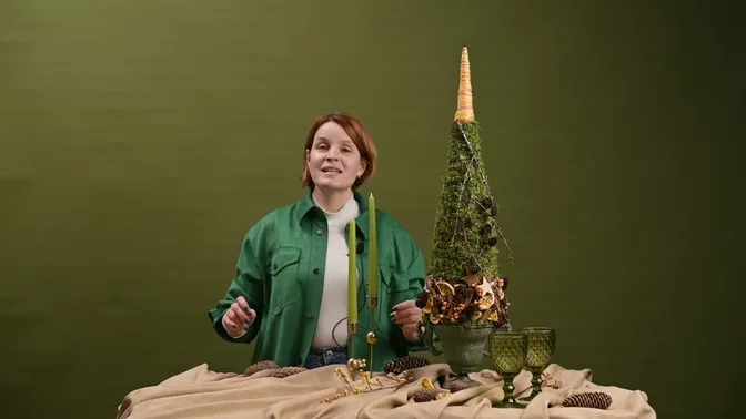 A tall moss-covered tree in a footed pot, with a yellow wrapped point and a lower band of dried citrus, cinnamon, cones and wooden stars.