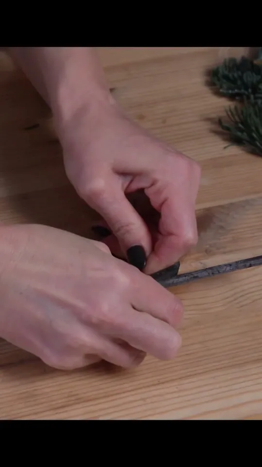 Hands securing wire around the crossing of two twigs