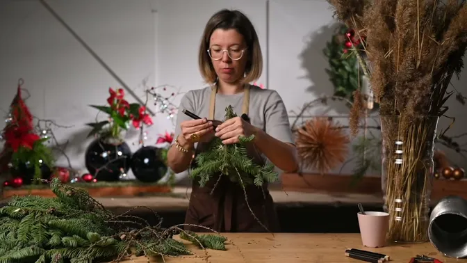 The maker binding an evergreen bundle with wire for a larger garland