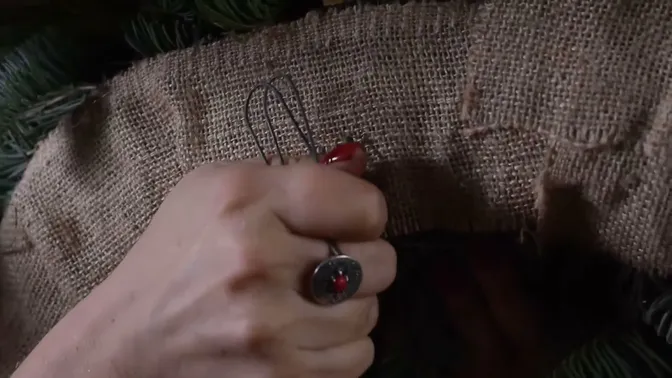 Wire loops on the coarse woven backing of the red-apple wreath, partly held by a hand