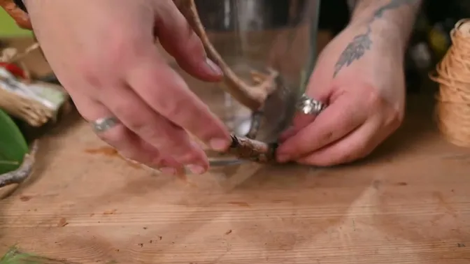 Hands holding a branch against the lower outside wall of the glass vase.