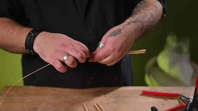 Hands wrapping wooden skewers with thin brown paper-covered wire.