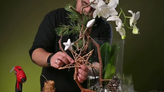 An open star made from wrapped skewers held against the branches below the white orchid flowers.