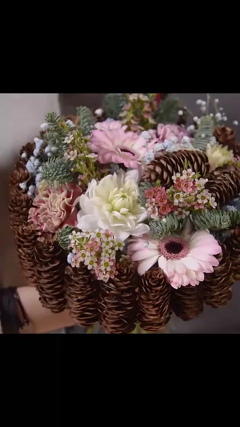 A compact winter bouquet with pale pink flowers and blue gypsophila held within a close rim of upright cones.