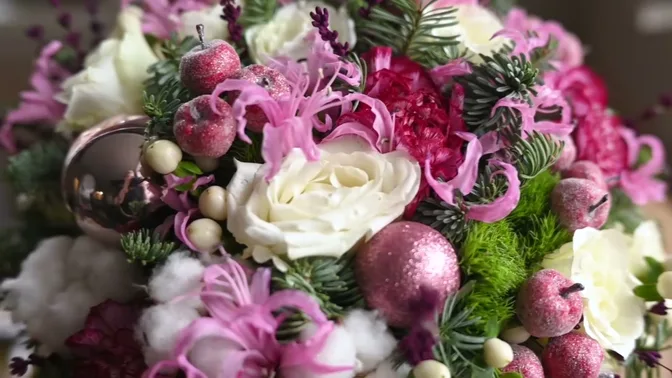 Close detail of white roses, pink nerines, carnations, cotton, berries, fir and pink ornaments in a holiday bouquet.