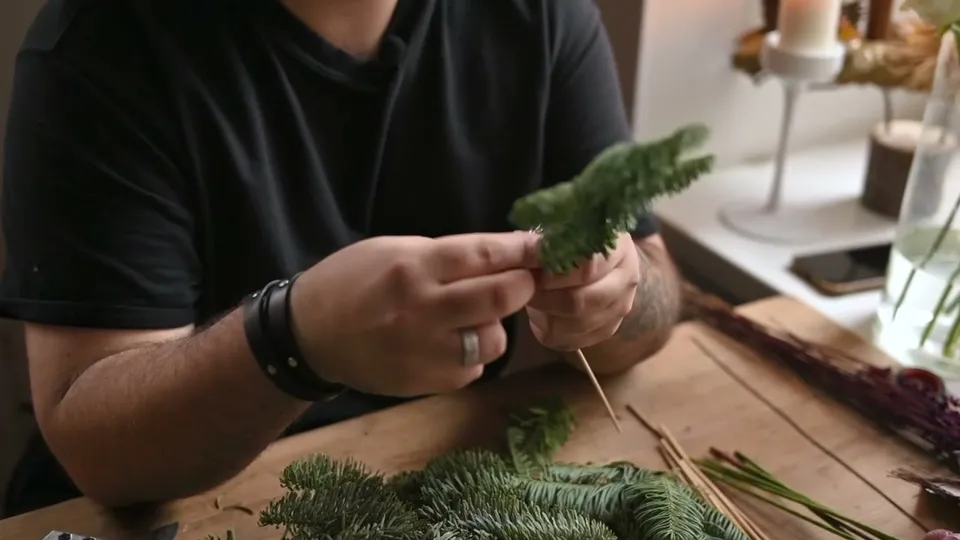 A short fir piece held alongside a long wooden skewer while green stem tape joins their stems.