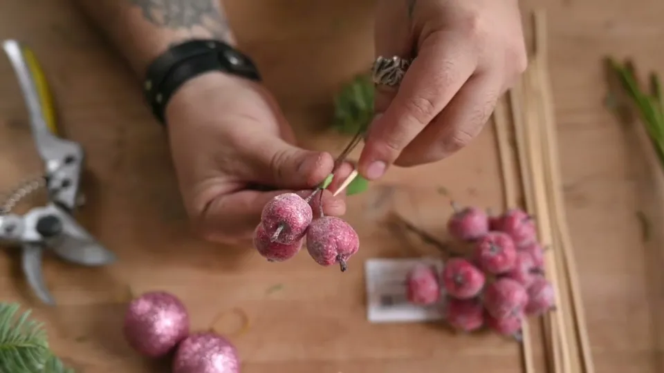 Two pink decorative apples on wire held beside a wooden skewer, with green tape around the join.