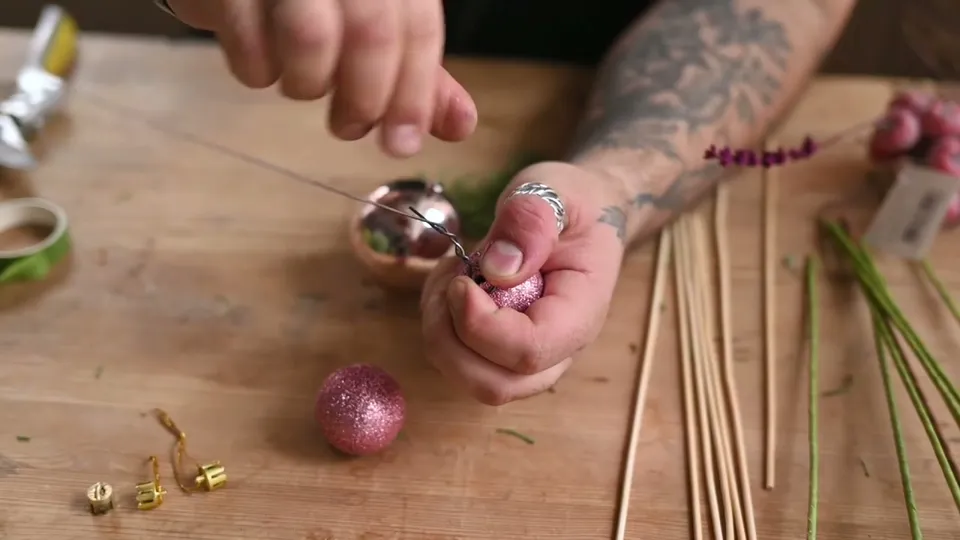 Wire twisted beneath the open neck of a pink bauble; removed hanging caps lie on the table.