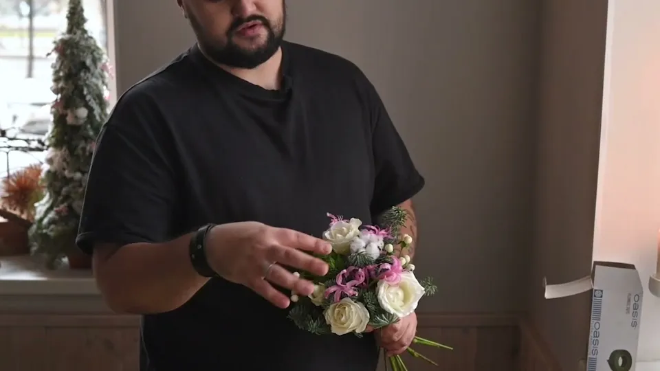 An emerging rounded bouquet of roses, pink flowers, cotton and fir held above a spreading bundle of stems.