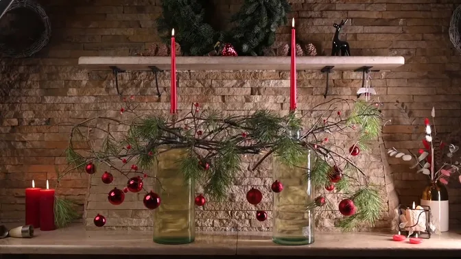 Two tall glass vessels connected by pine and bare branches, with red baubles and a central white flower.