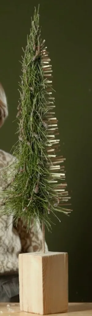 Slender Christmas tree of pine needles and reeds on a square wooden base.