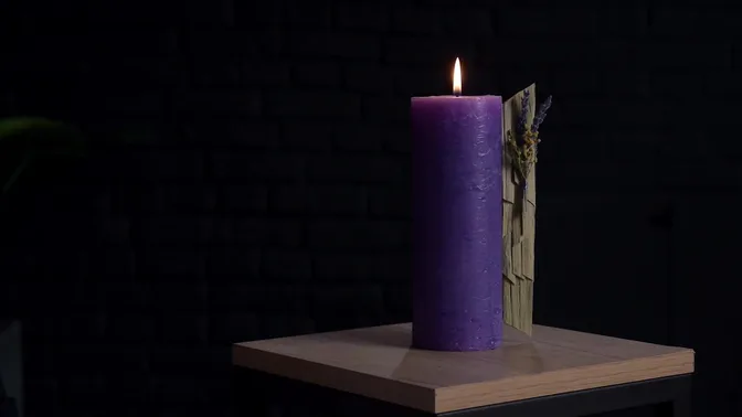 Purple decorative candle beside a panel of dry leaves with lavender and mimosa.