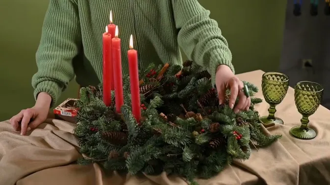 Rustic evergreen table wreath with four red candles and natural decorations.