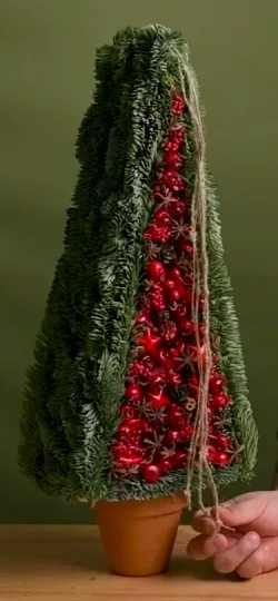 Tall triangular evergreen frame with red decorations and twine in a terracotta pot.