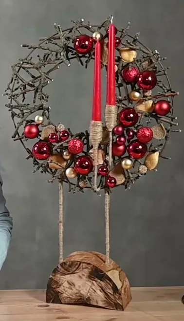 Open branch wreath with red and gold baubles, two decorative candles and a wooden stand.