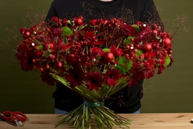 Wide red Christmas bouquet with baubles on a circular yarn-wrapped frame.