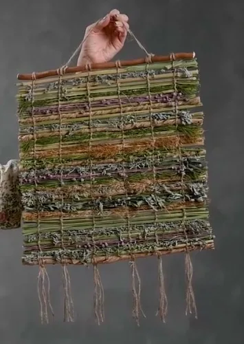 Natural wall hanging with woven bands of grasses and dried stems, a wooden hanging rod and loose tassels.
