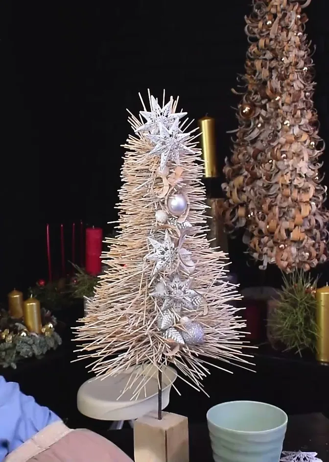 Open white wire and rattan Christmas tree with a star and silver baubles on a wooden stand.