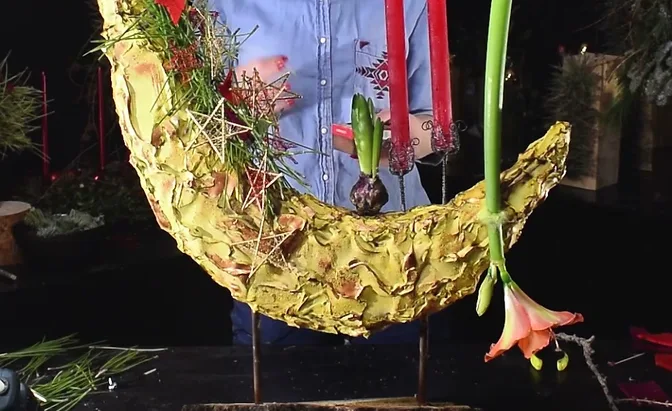 Close-up of a gold crescent arrangement with wire stars, red candles and a pink amaryllis flower.