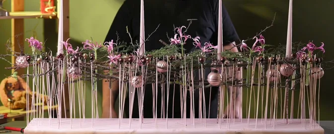 Airy Christmas arrangement of pink flowers, fine stems and pale candles on a long wooden board.