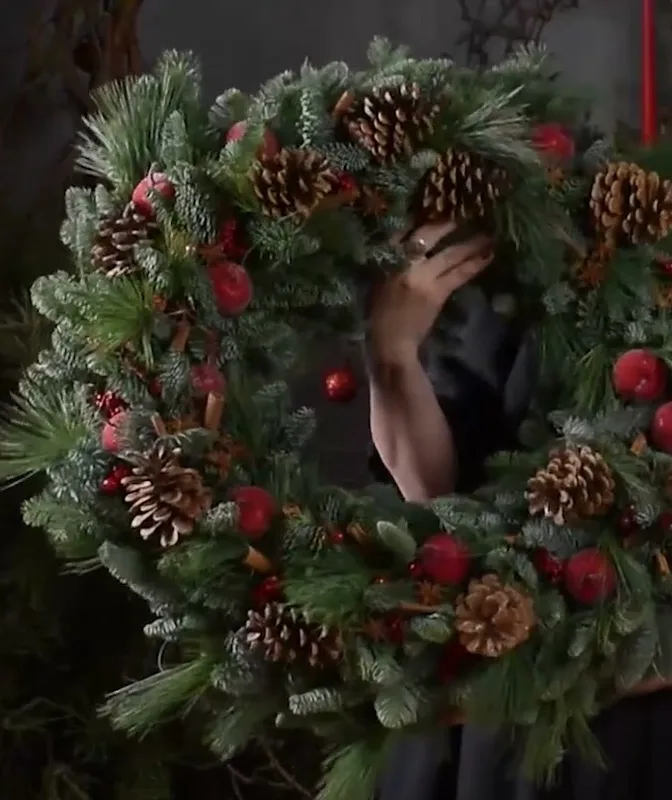 Close-up of an evergreen Christmas wreath decorated with pinecones, red accents and dried fruit.