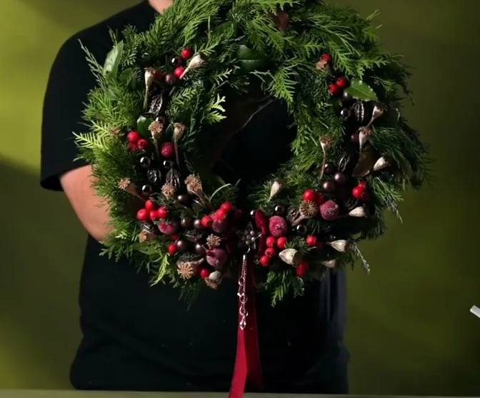 Evergreen door wreath with red berries, gold details and a long red velvet bow.