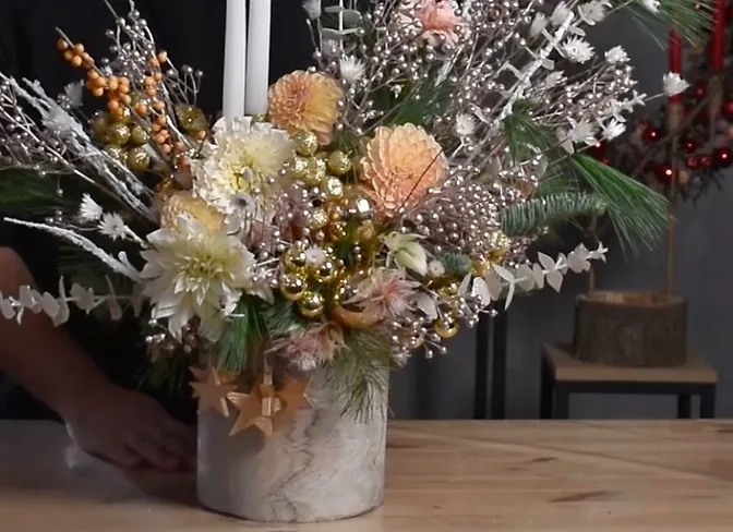 Asymmetrical arrangement with evergreen branches, pale flowers and tall candles in a light-coloured pot.