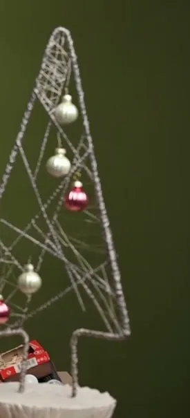 Open wire Christmas tree decorated with baubles on a white plaster base.