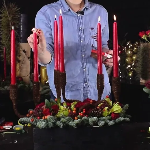 Christmas flower arrangement with evergreen branches, red berries and tall red candles in a wooden box.