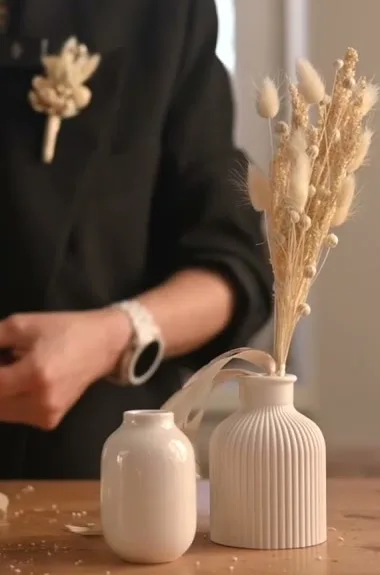 Small dried-flower bouquet in a ribbed cream ceramic vase beside a smaller matching pot.